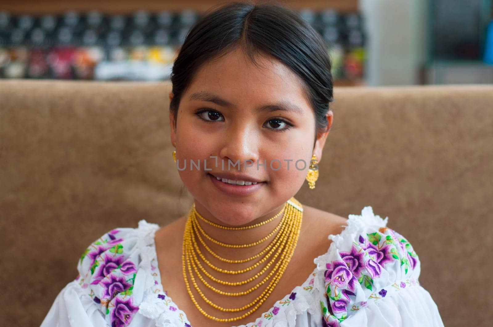 closeup of beautiful young woman in traditional dress and gold necklaces sitting in a coffee shop smiling at camera. High quality photo
