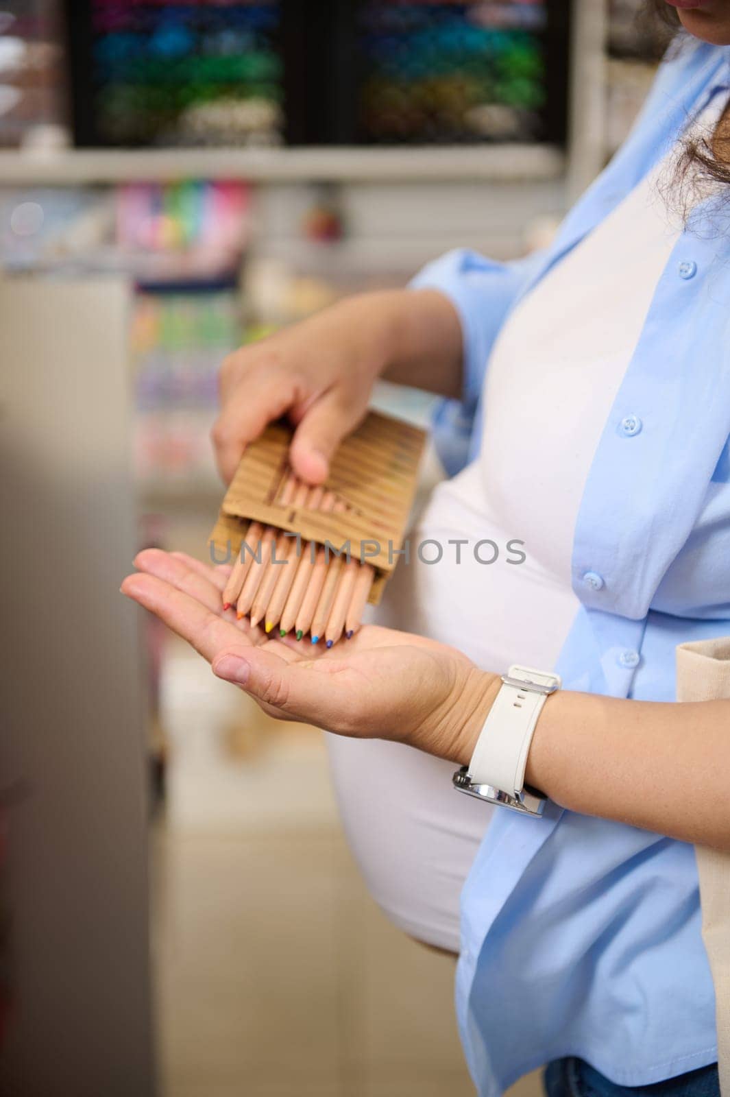 Stylish wooden color pencils in the hands of a pregnant woman shopping for school supplies in school stationery store by artgf