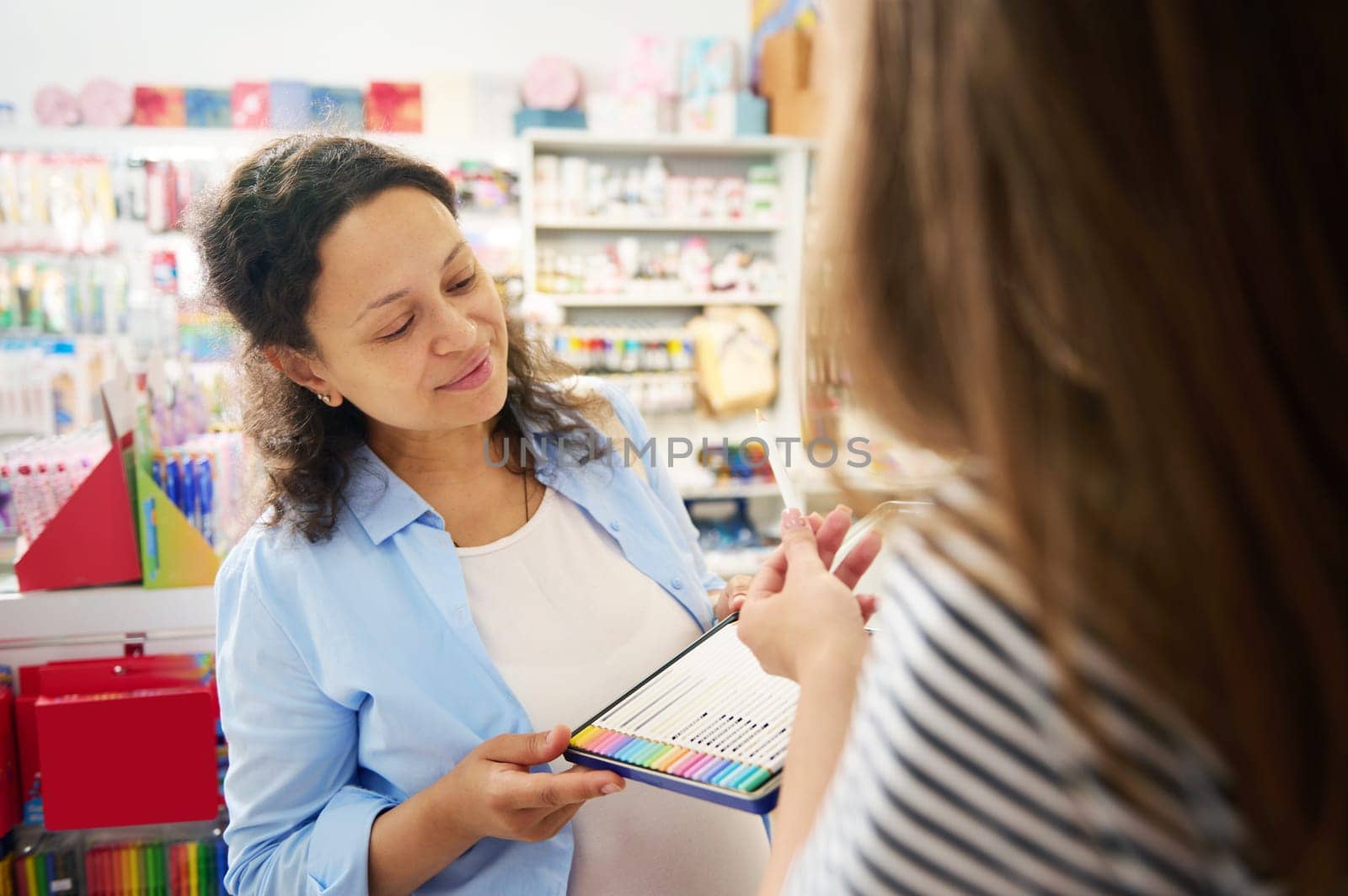 Smiling multi-ethnic woman holding metal case with colored pencils, shopping for school stationery in creative art store. Office supply supermarket. Hobby, creativity, art. Back to school concept