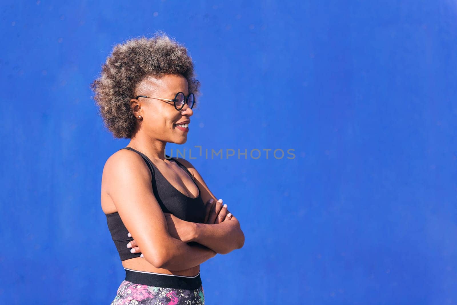 Profile of a strong african american sportswoman in a blue background outdoors in a sunny day, concept of real people and sporty lifestyle, copy space for text