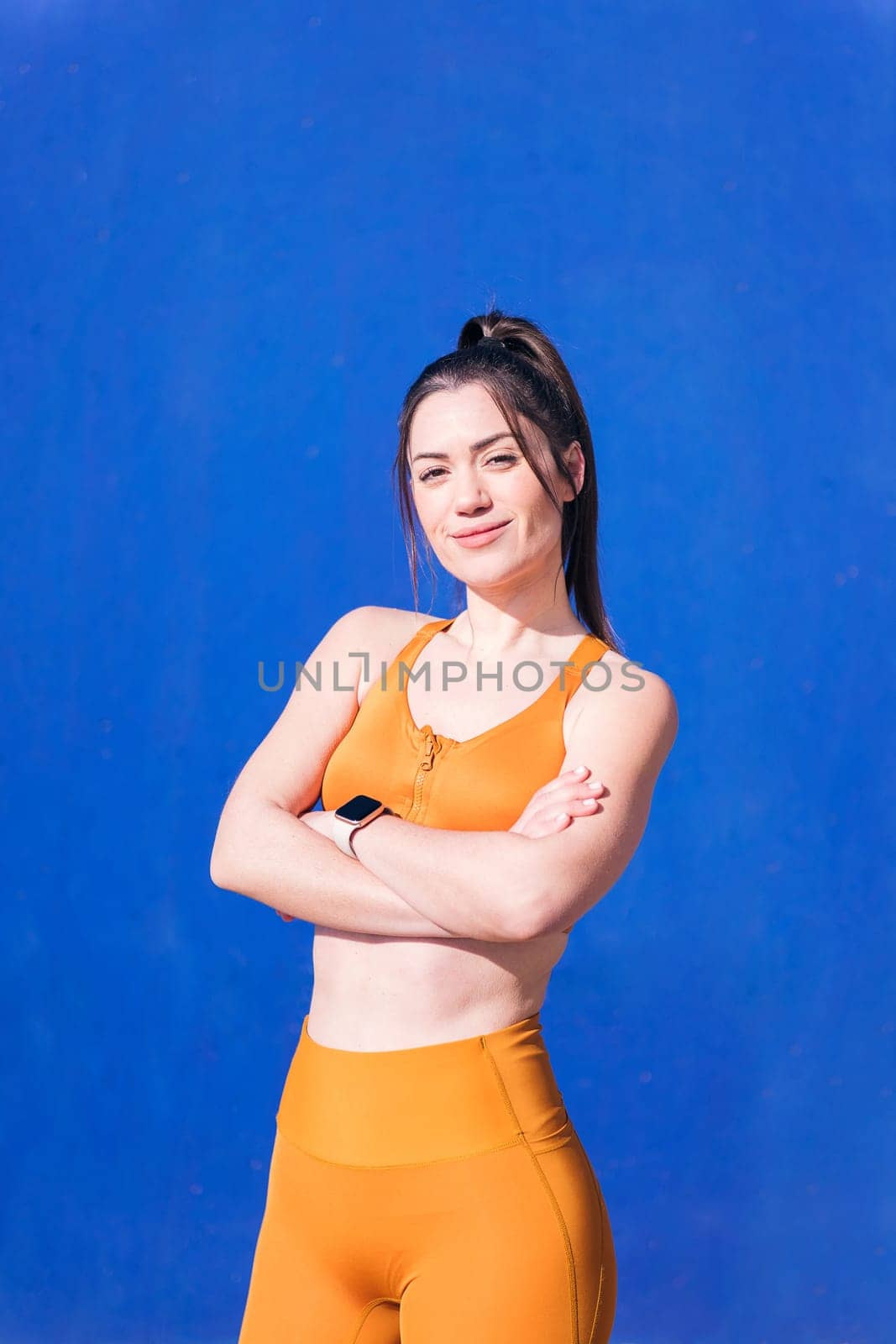 vertical portrait of a smiling caucasian sportswoman in a blue background outdoors in a sunny day, concept of real people and sporty lifestyle, copy space for text