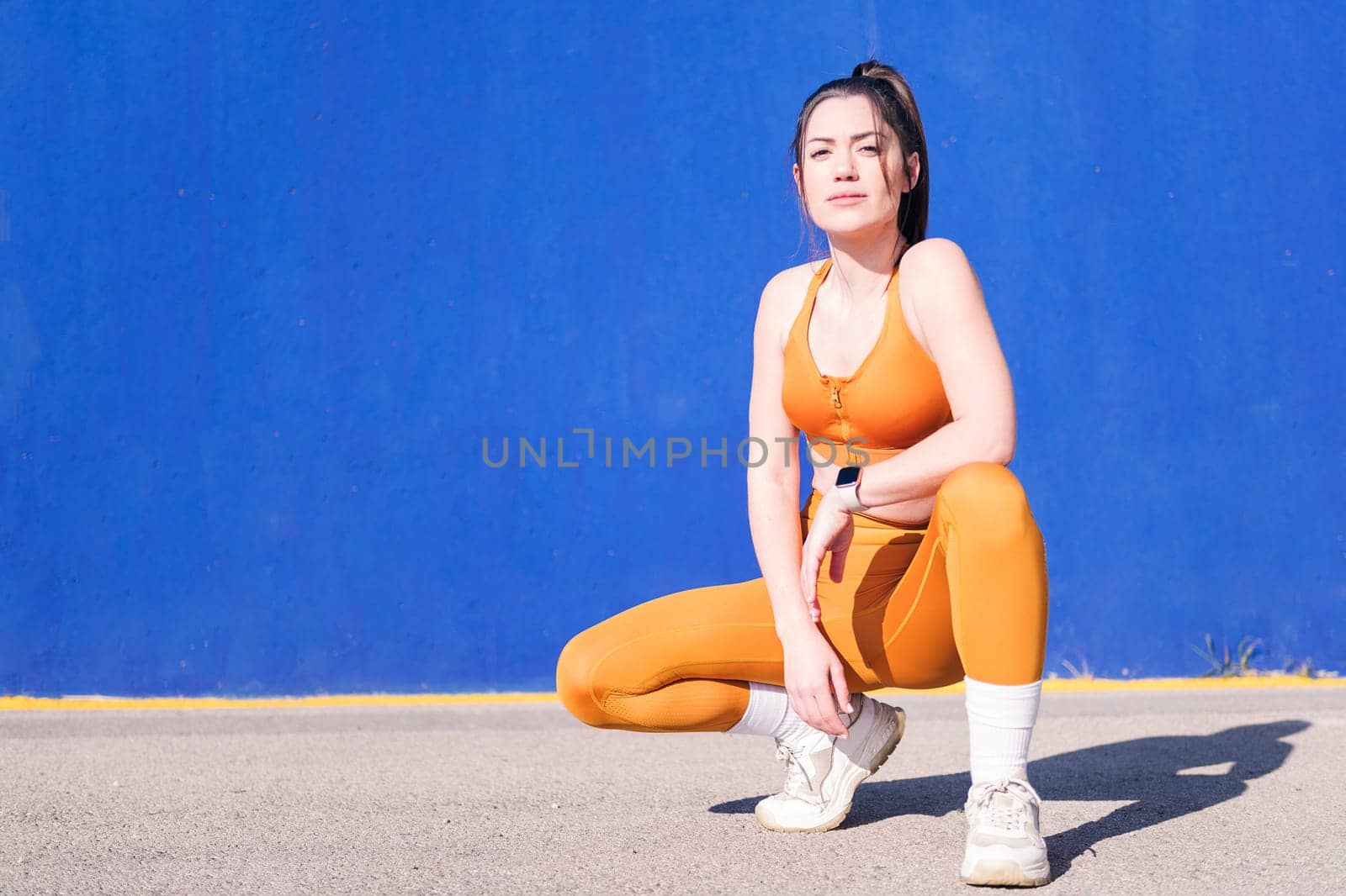 sportswoman squatting while posing on the street in a blue background, concept of sport and healthy lifestyle, copy space for text