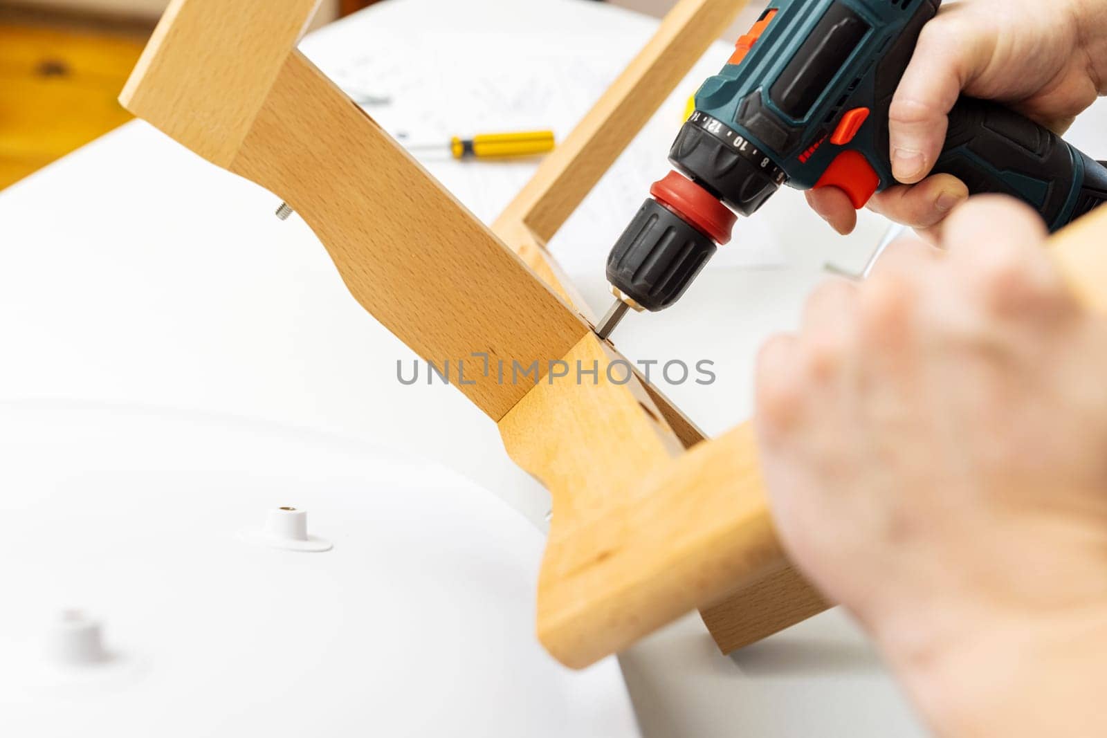 Craftsman collecting and repairing with tools, assembling furniture with drill. Man screws details to chair with electric screwdriver at home after renovation