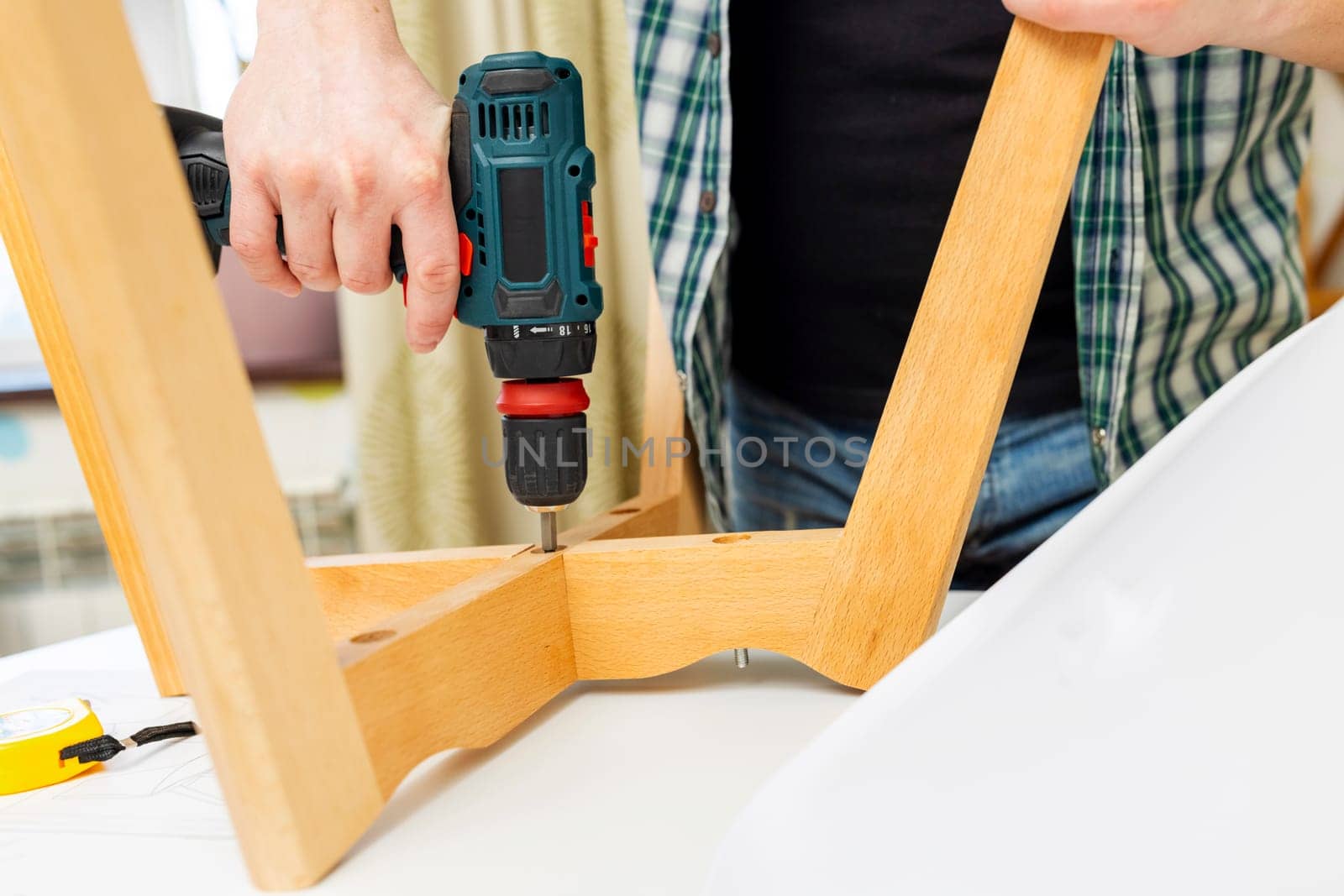 Craftsman collecting and repairing with tools, assembling furniture with drill. Man screws details to chair with electric screwdriver at home after renovation