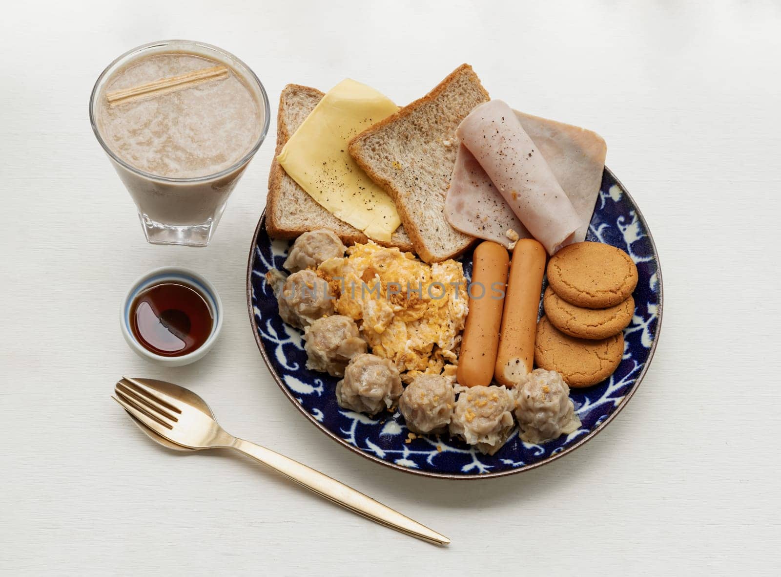 Homemade breakfast is including Breads, Fried sausages, Ham, Pork shumais, Scrambled eggs, Cheese, Crispy ginger cookies and Honey served with Cup of Healthy Protein Shake with white background. Healthy food concept, Space for text, Selective Focus.