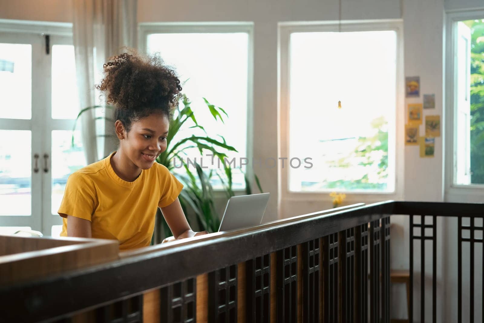 Young African American woman wearing casual clothes working remotely, surfing internet on laptop while sitting in cafe.