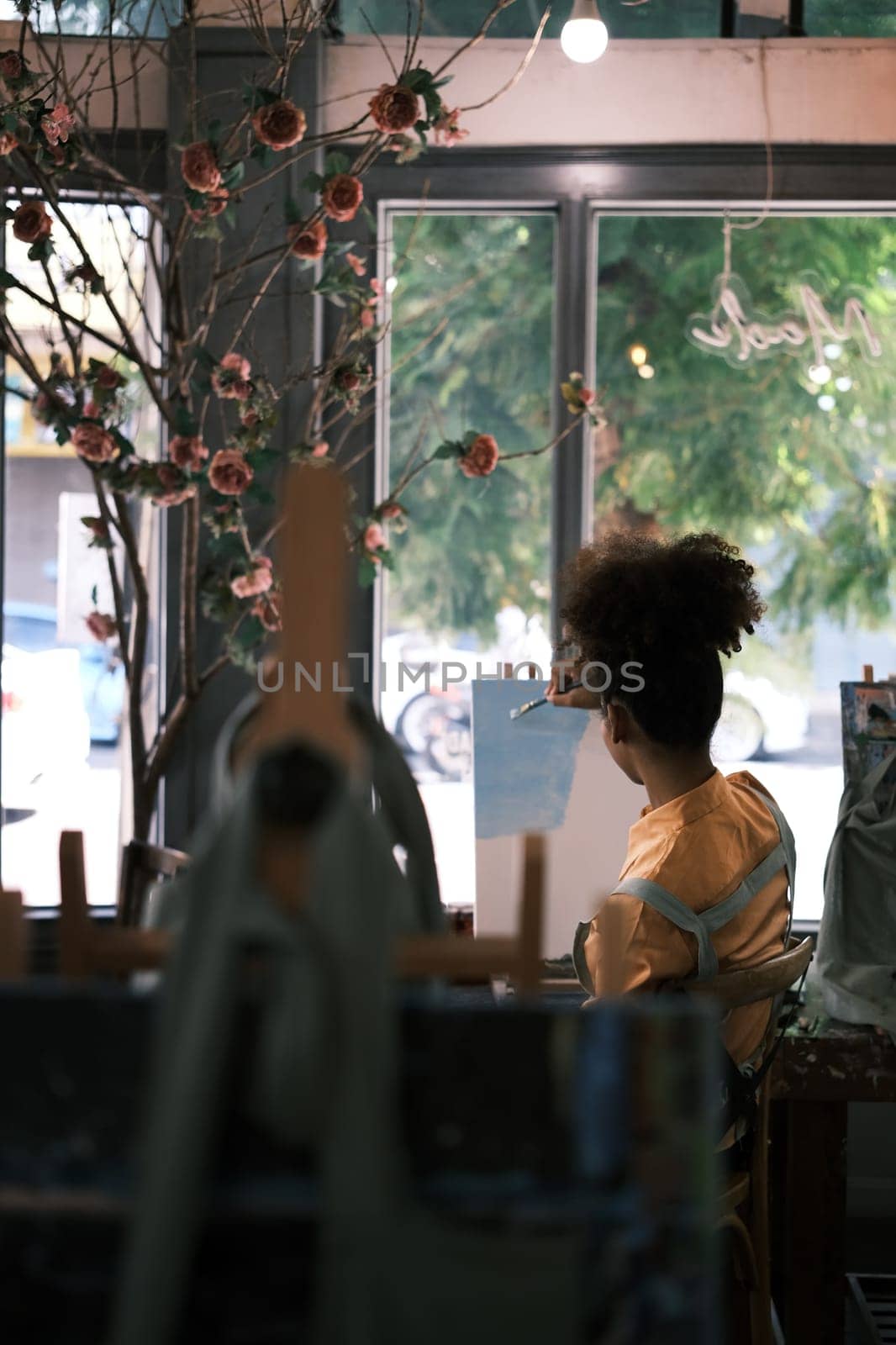 Rear view of female artist sitting in front of an easel and creating artwork on canvas in art studio.