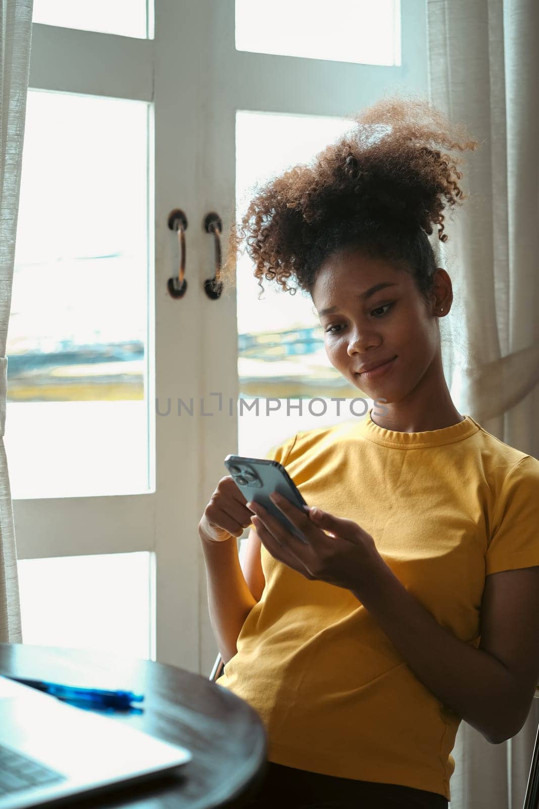 Pleasant young woman sitting in bright living room and typing text massage on smartphone.