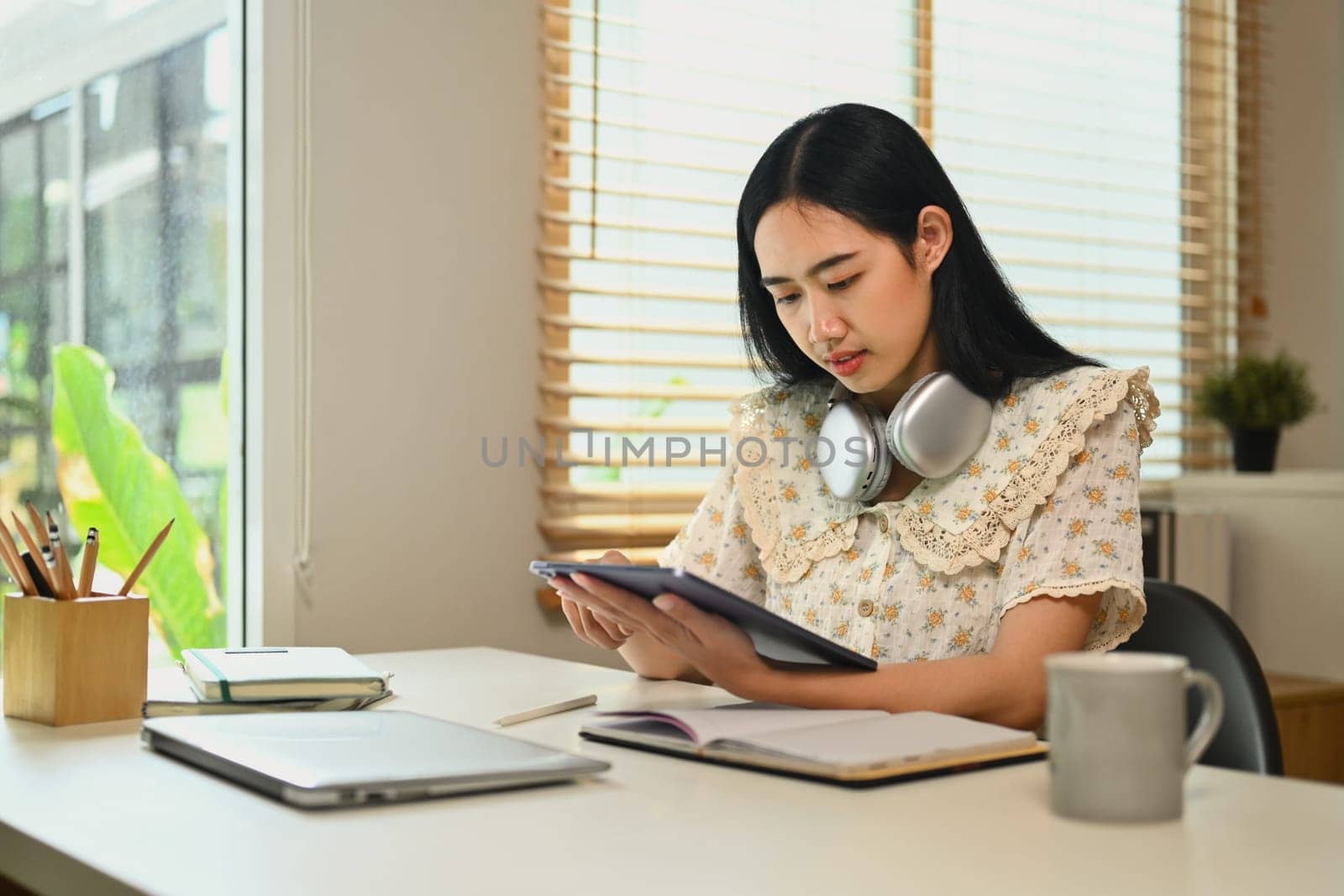 Pretty young Asian woman using digital tablet and making notes, browsing internet, remote work and stying online.