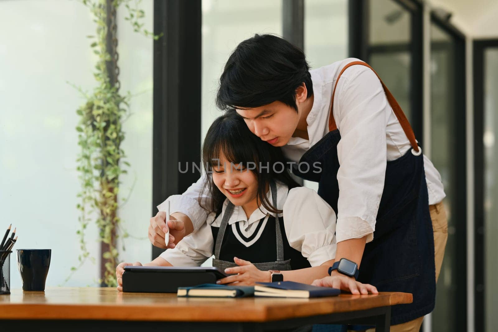 Happy young couple using digital tablet and working together at their coffee shop. Small business management concept.