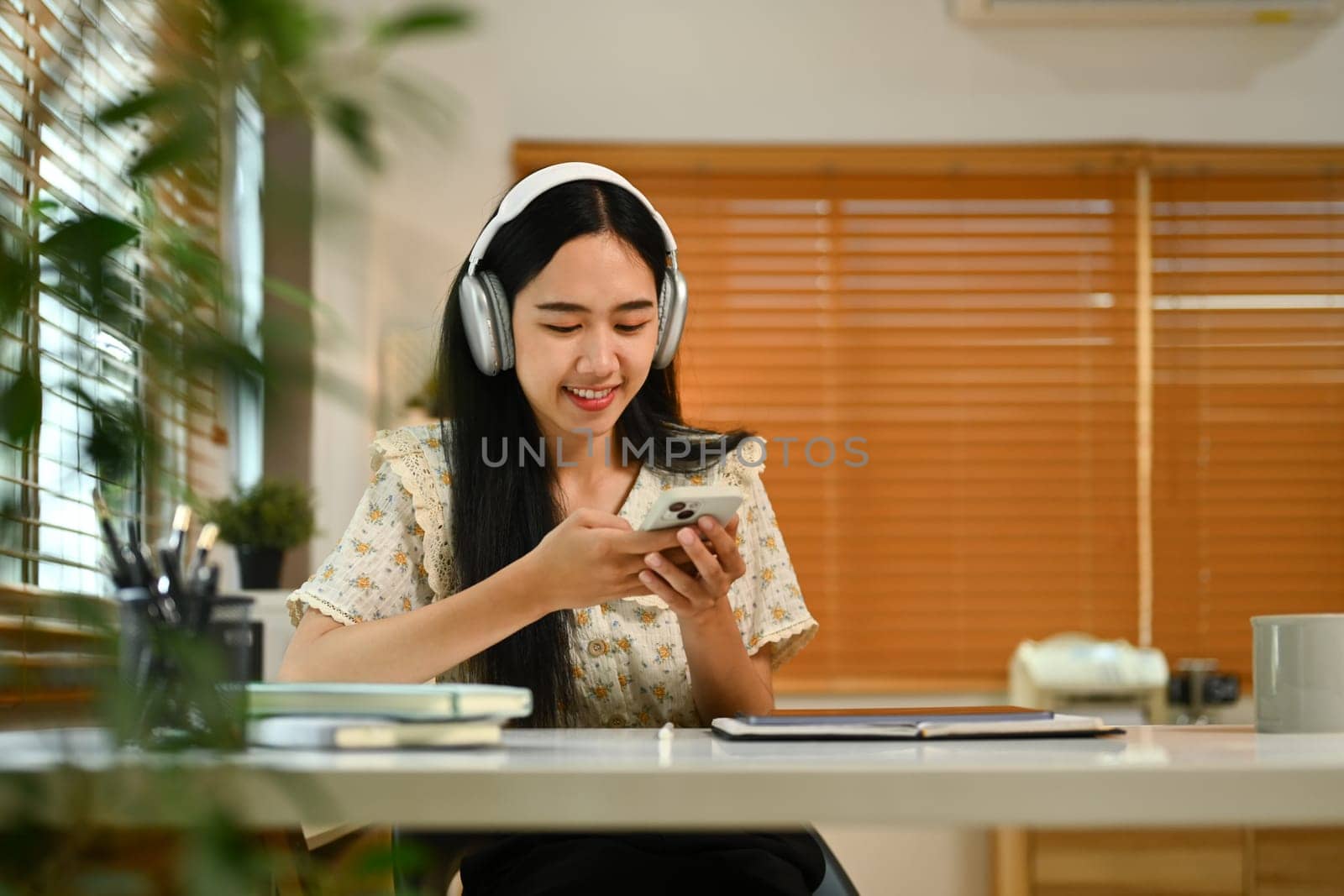 Teenage asian woman sitting at cozy home interior, chatting with friends in social media on smartphone.