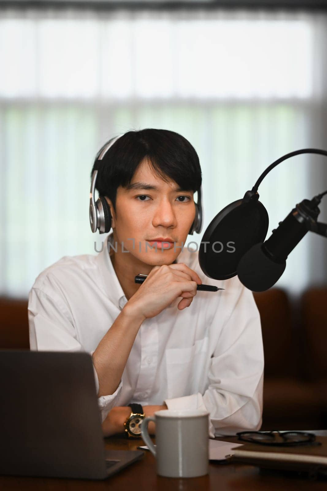 Image of male radio host listening to interesting conversation with guest during recording podcast in home studio by prathanchorruangsak
