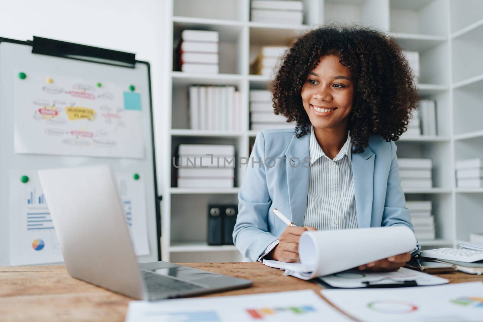 Beautiful young African american businesswoman using laptop computer and paperworks with planning working on financial document, tax, exchange, accounting and Financial advisor by Manastrong