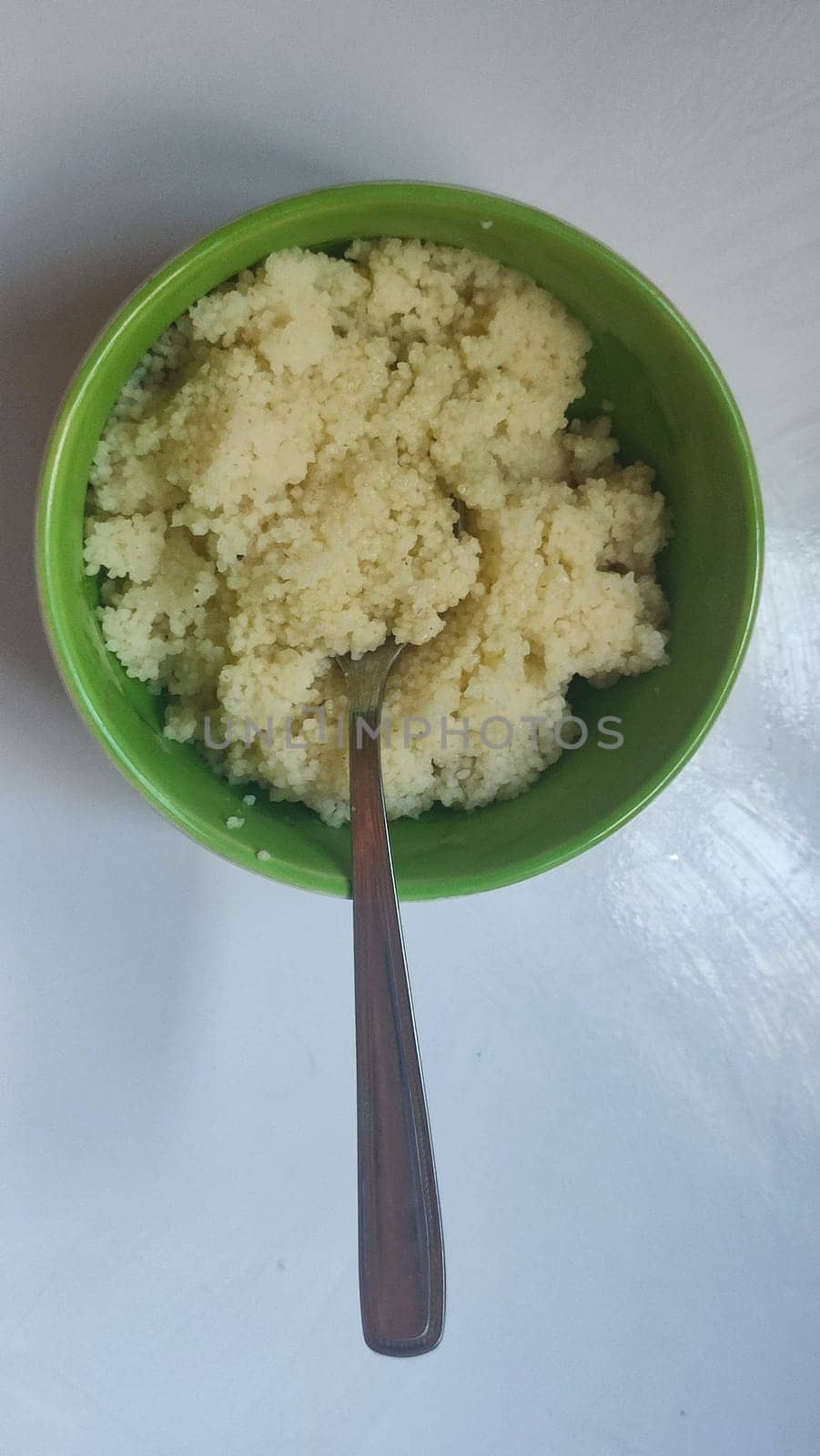 boiled couscous porridge in a green deep plate with a spoon, homemade food. High quality photo
