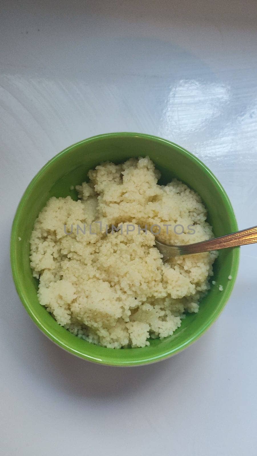 boiled couscous porridge in a green deep plate with a spoon, homemade food. High quality photo