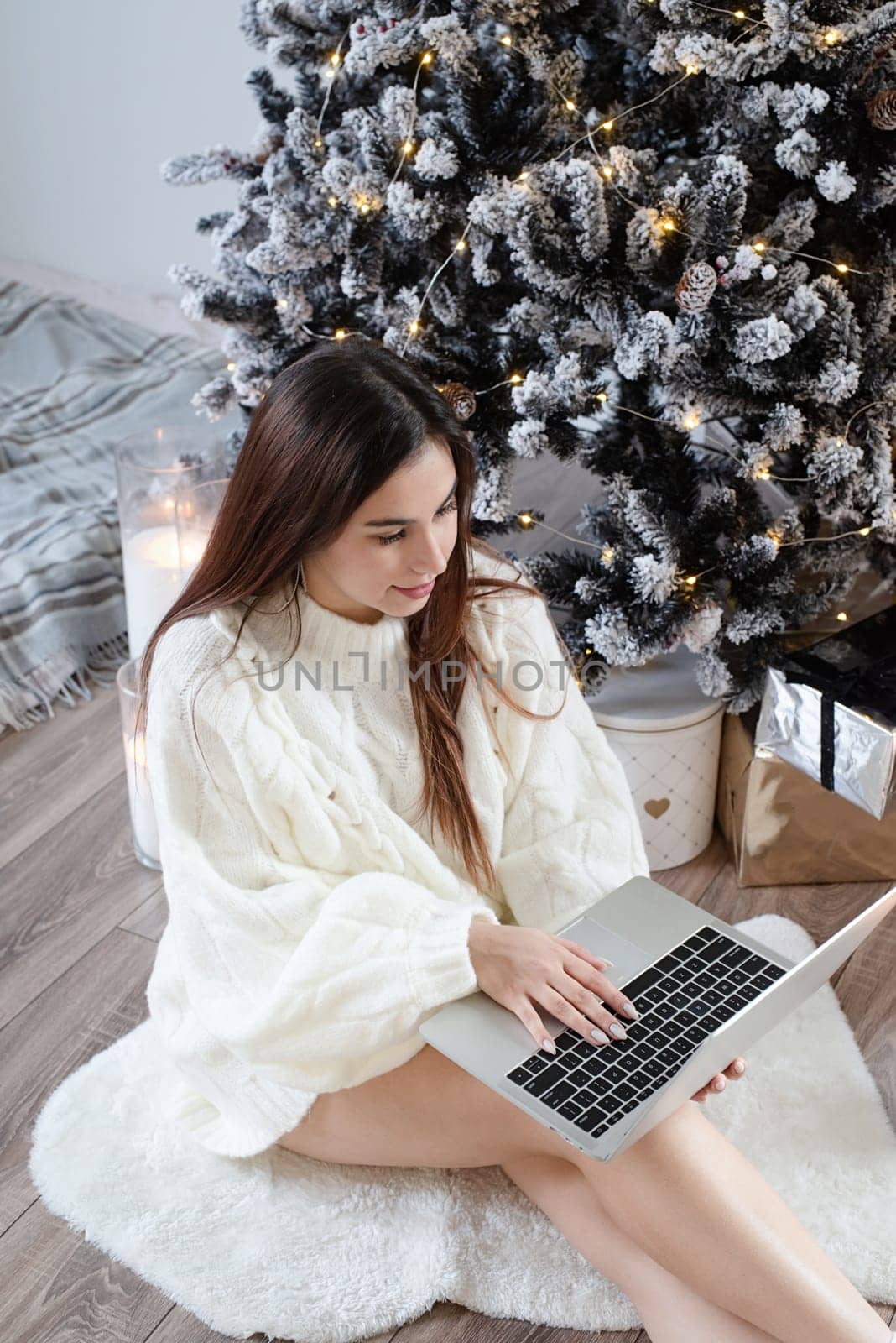 Merry Christmas and Happy New Year. Woman in warm white winter sweater lying in bed at home using laptop, watching movies or working