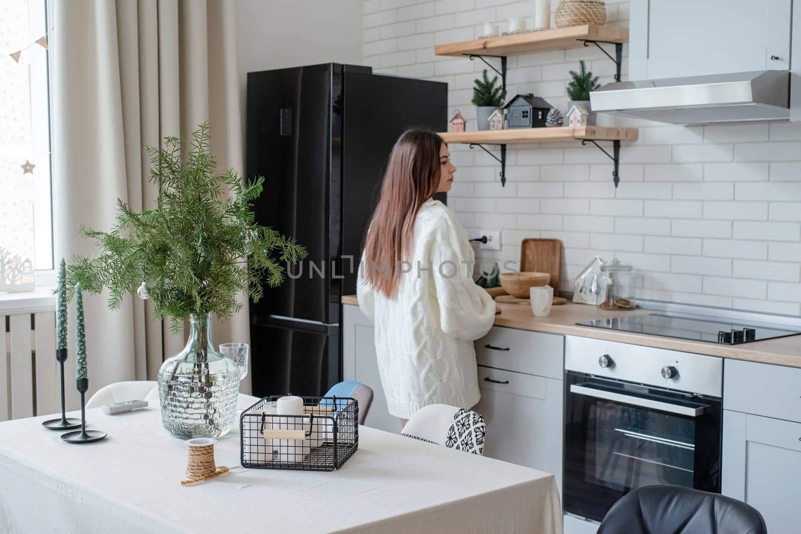 Merry Christmas and Happy New Year. Woman in warm white winter sweater standing at the kitchen at home