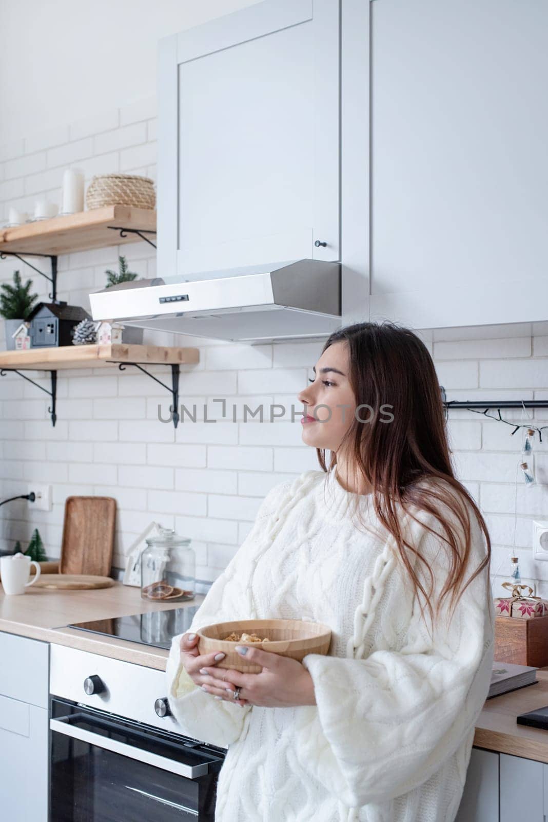 Woman in warm white winter sweater standing at the kitchen at home by Desperada