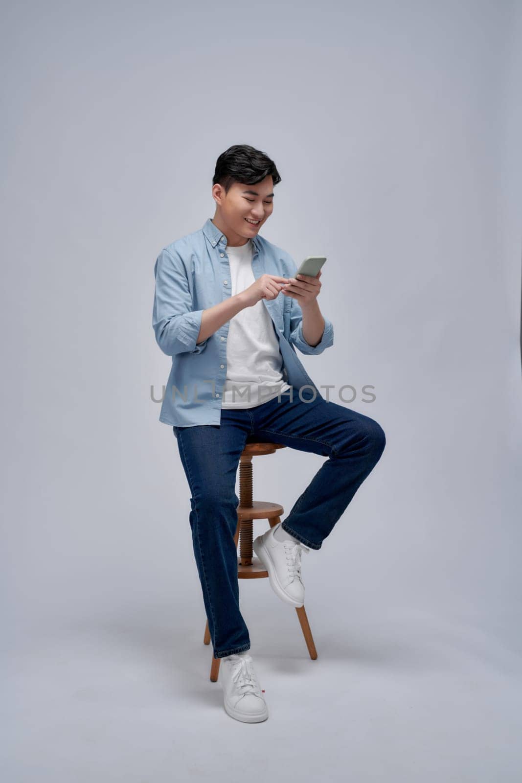 Handsome attractive man using a mobile phone and sitting on a chair isolated on white background by makidotvn