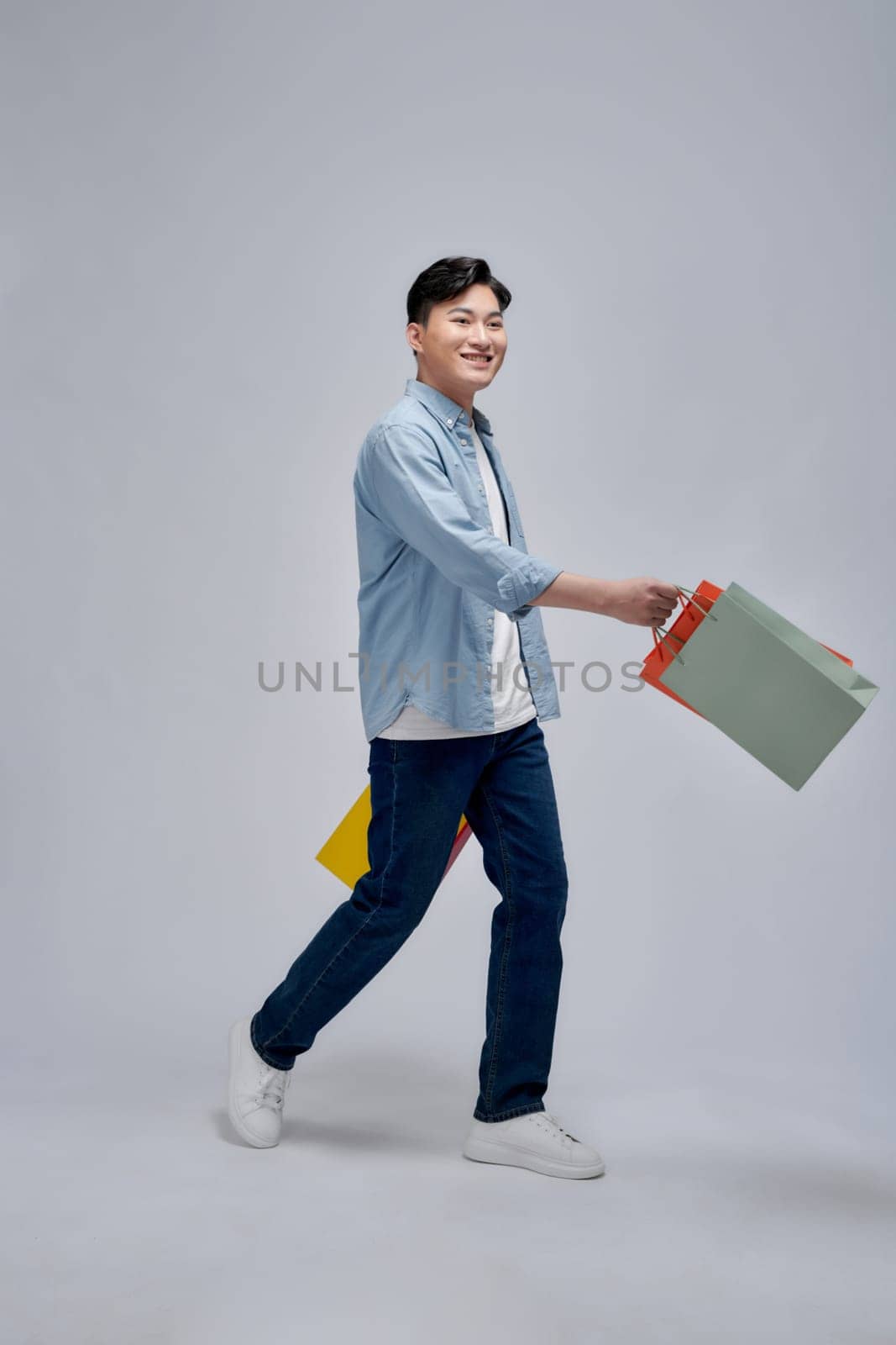 Young positive man hold bags from shopping store advert satisfied