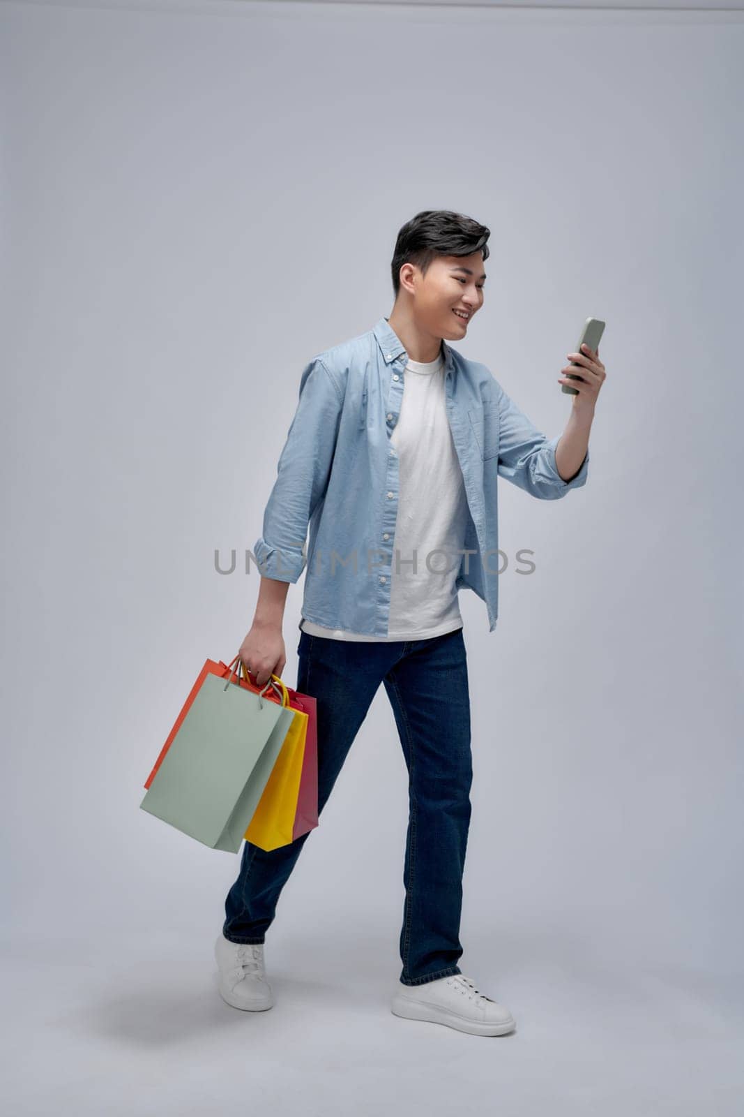 Young Asian man with shopping bags is using a mobile phone and smiling while doing shopping
