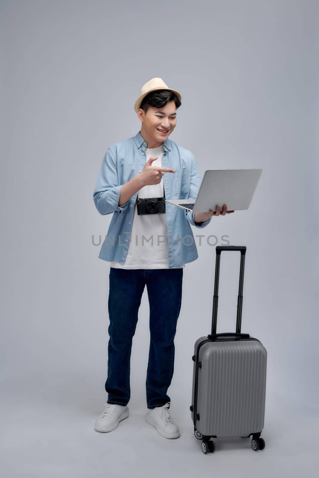 Young guy standing with luggage suitcase browsing internet on laptop concentrated smiling joyful by makidotvn