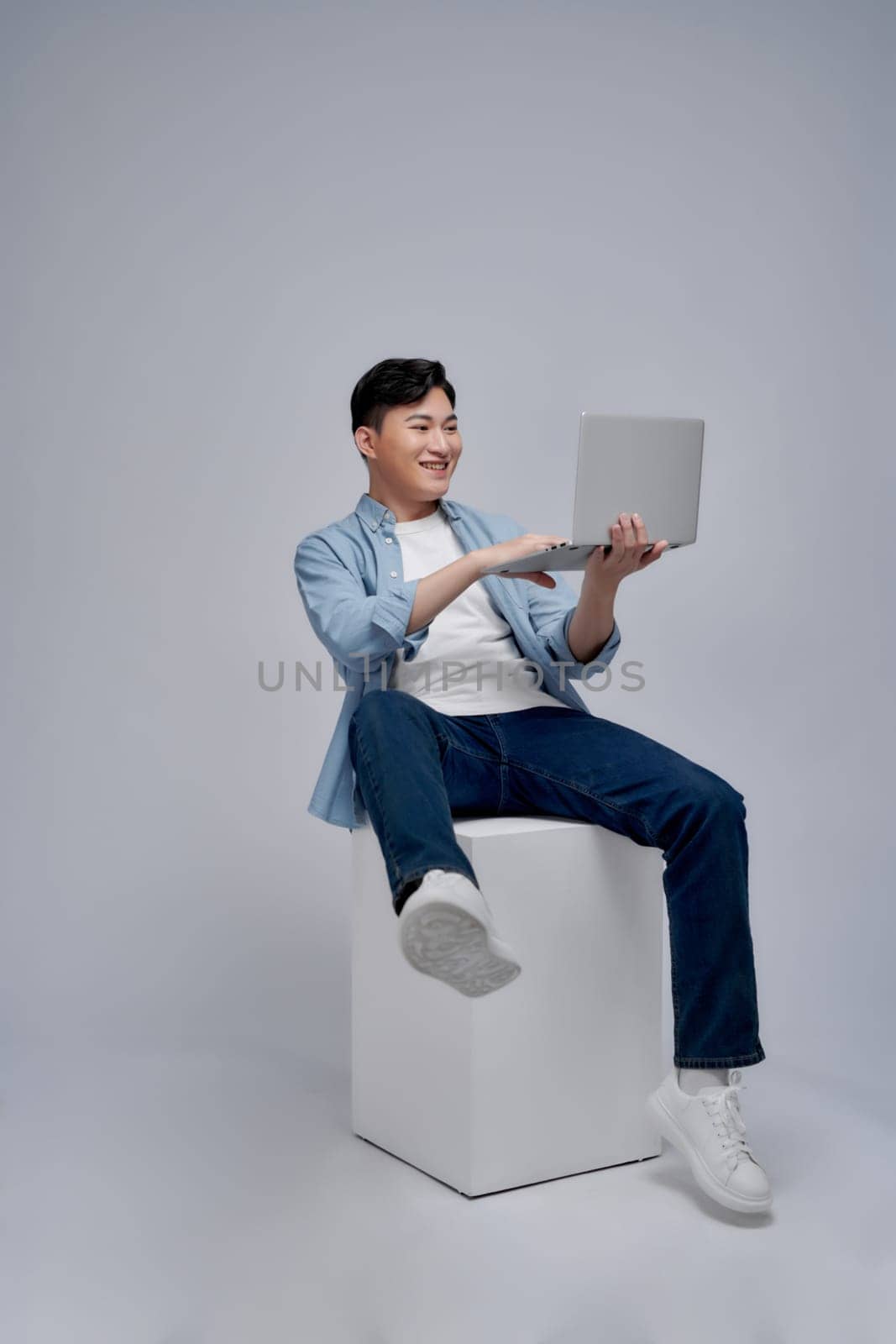 Young Asian man sitting and using laptop on white background by makidotvn