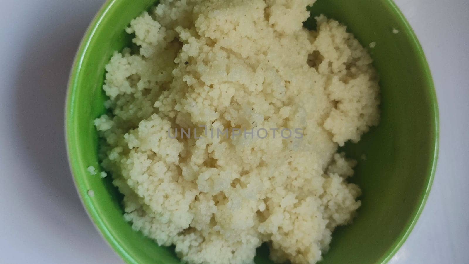 boiled couscous porridge in a green deep plate with a spoon, homemade food. High quality photo