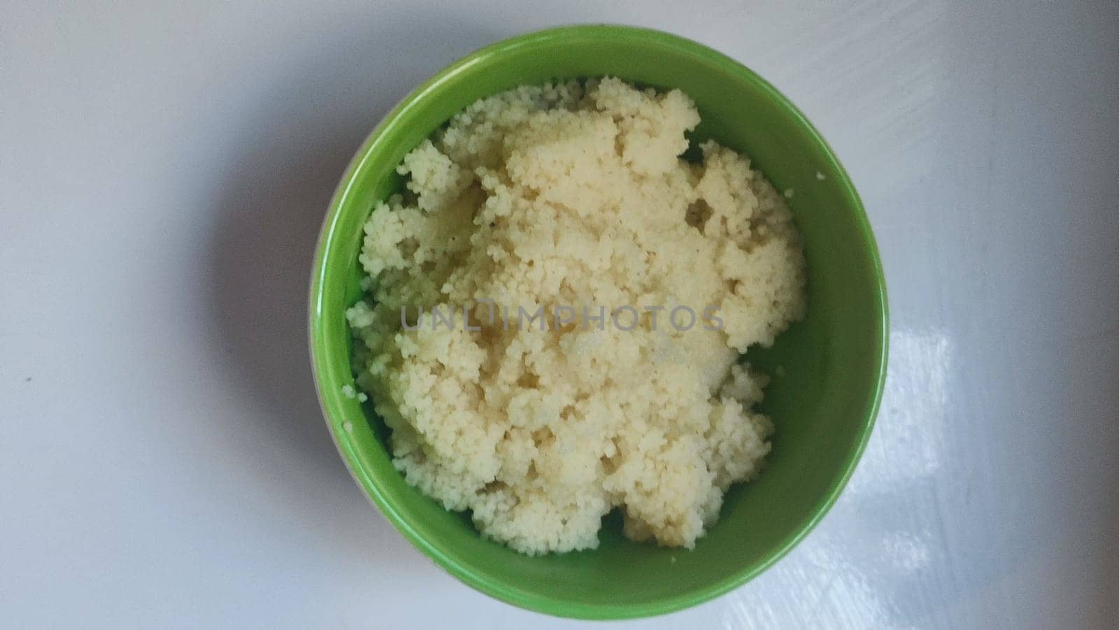 boiled couscous porridge in a green deep plate with a spoon, homemade food. High quality photo