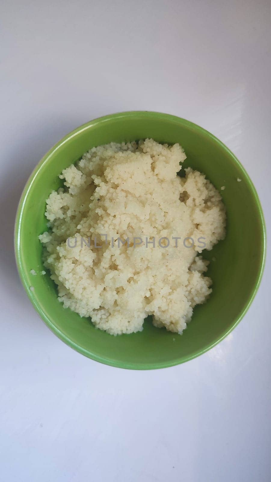 boiled couscous porridge in a green deep plate with a spoon, homemade food. High quality photo