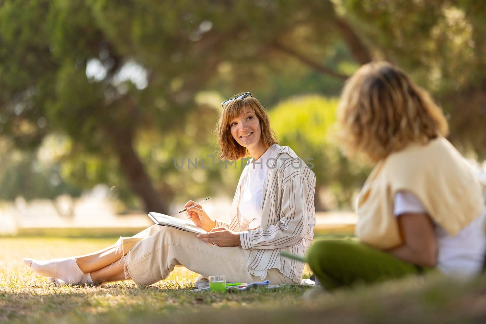 Two women painting in the blooming park and looking at each other by Studia72