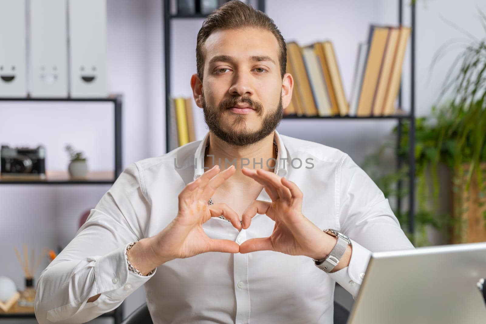 I love you. Lebanese business man makes symbol of love, showing heart sign to camera, express romantic feelings express sincere positive feelings at home office workplace. Charity, gratitude, donation
