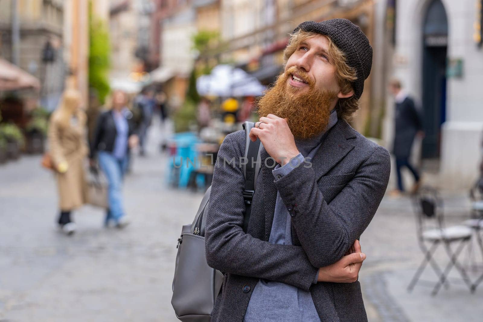 Thoughtful pensive puzzled man with pensive expression, pondering a solution, doubting question, thinking inspiration dreaming outdoors. Redhead guy in city street pointing empty place. Copy-space