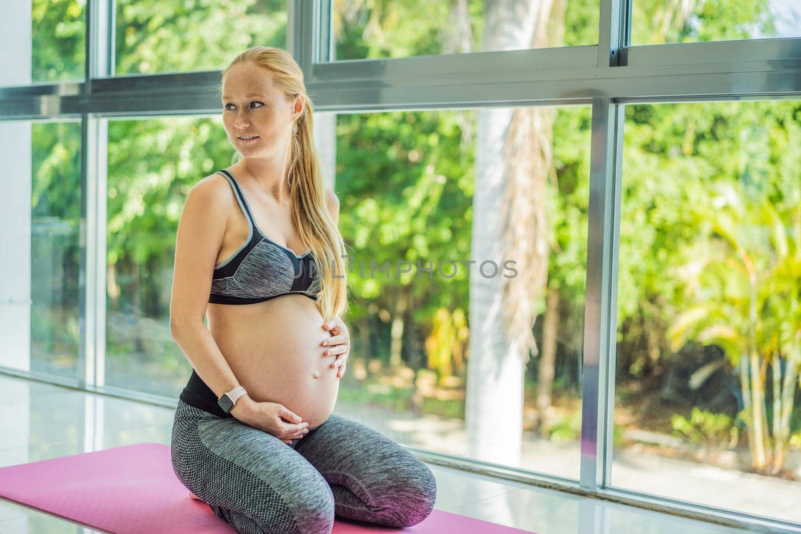 Young pregnant woman doing yoga exercises and meditating at home or yoga studio. Health care, mindfulness, relaxation and wellness concept.