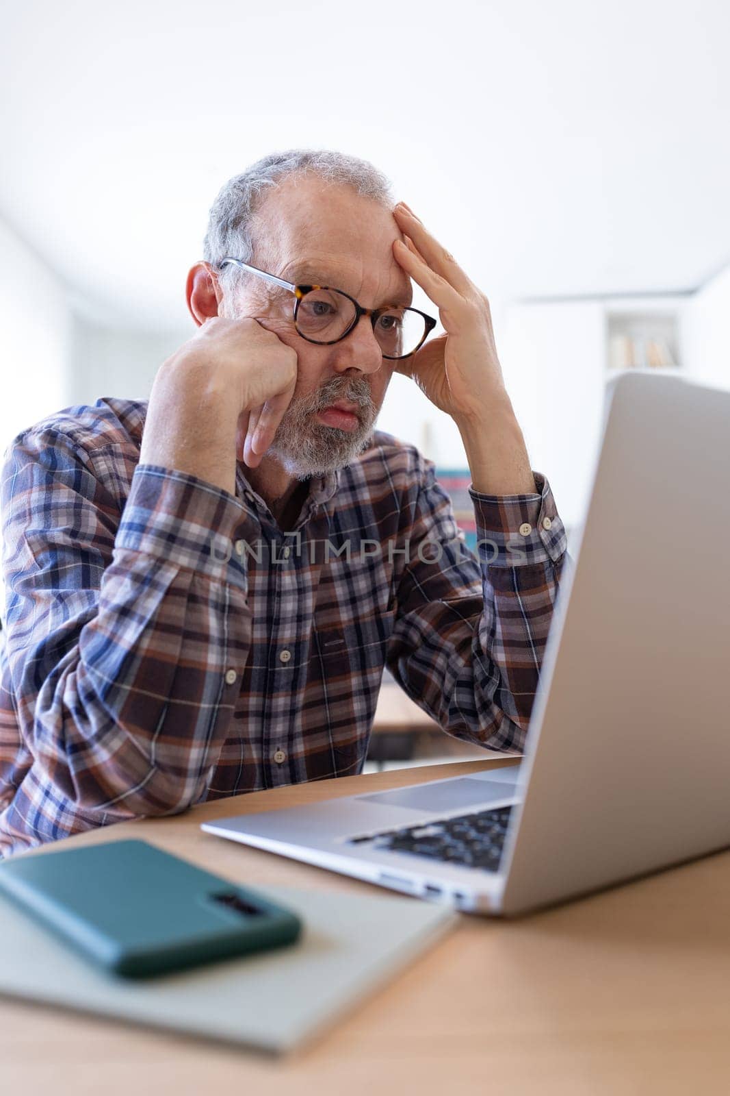 Stressed and disappointed senior caucasian man using laptop at home feeling overwhelmed. Vertical image. Technology.
