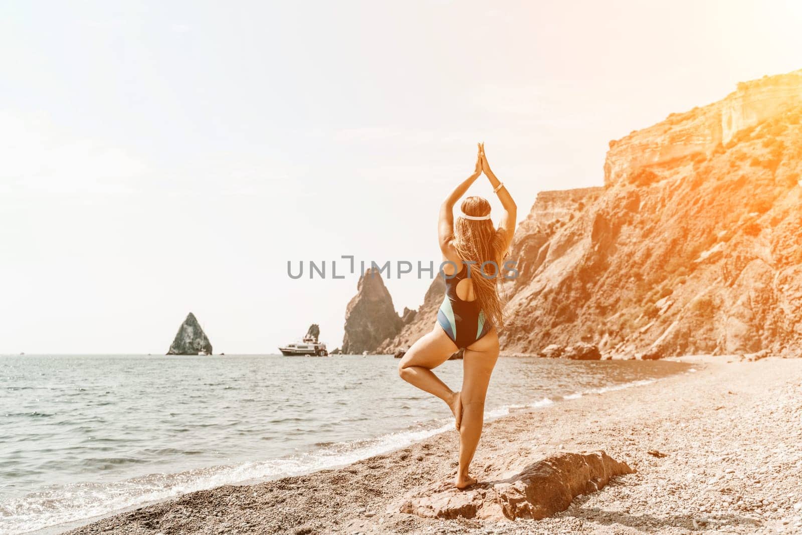 Yoga on the beach. A happy woman meditating in a yoga pose on the beach, surrounded by the ocean and rock mountains, promoting a healthy lifestyle outdoors in nature, and inspiring fitness concept. by Matiunina