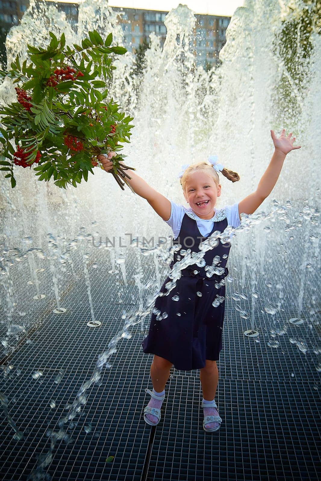 Little girl of elementary school student in modern school uniform outdoors near the fountain water jets. Female child schoolgirl having fun. Back to school in september 1 in Russia by keleny