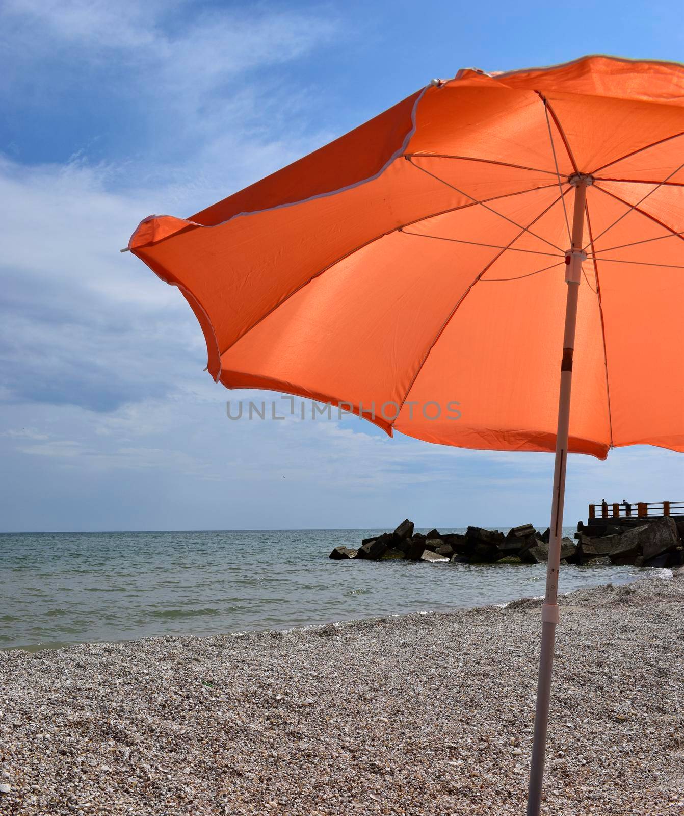 Orange beach umbrella near the sea in sunny day. Beautiful blue sky and clouds. Relaxation, vacation idyllic background.
