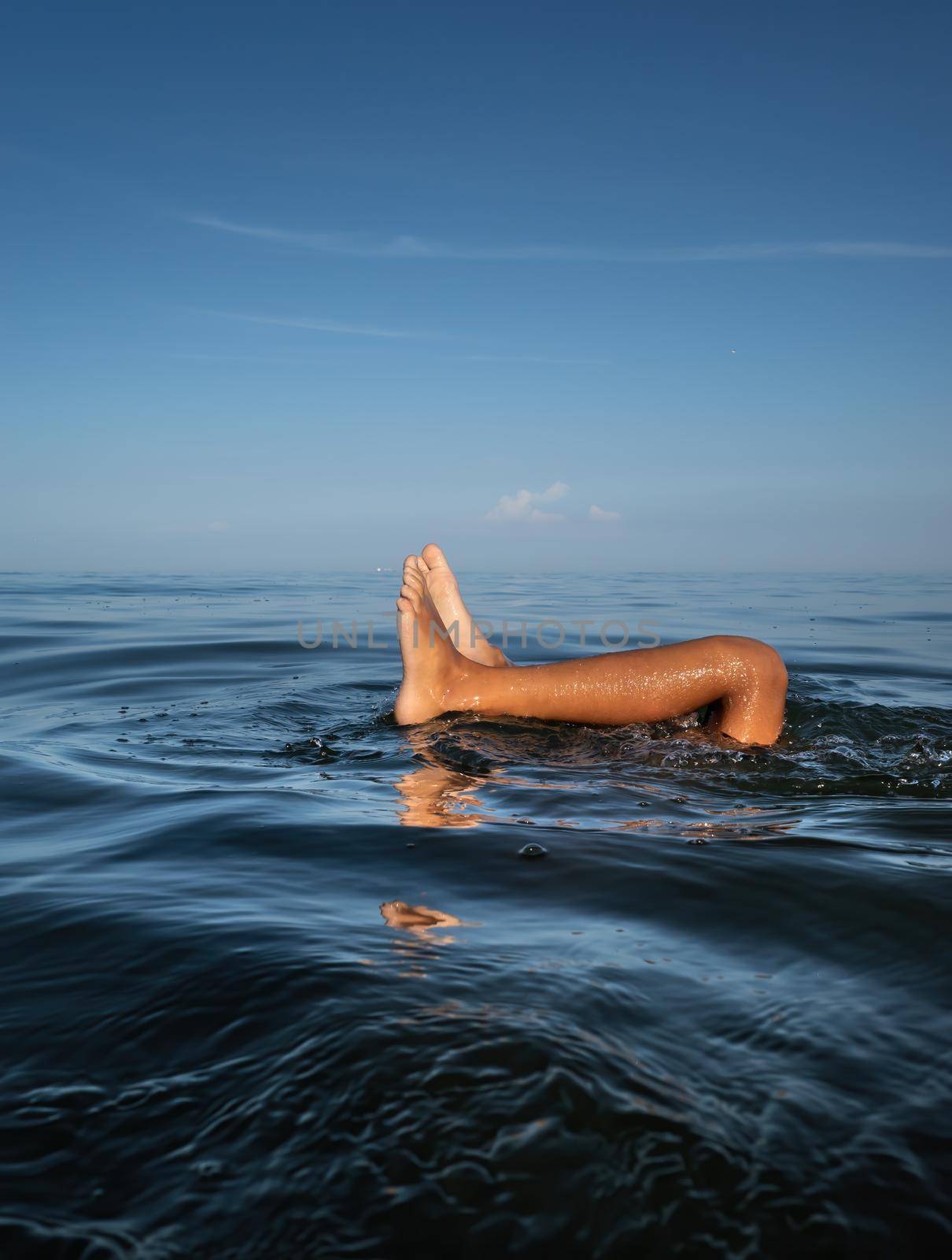 Relaxation and healthy lifestyle. Young boy teenager bathes in the sea. The boy dives and his legs stick out above the water