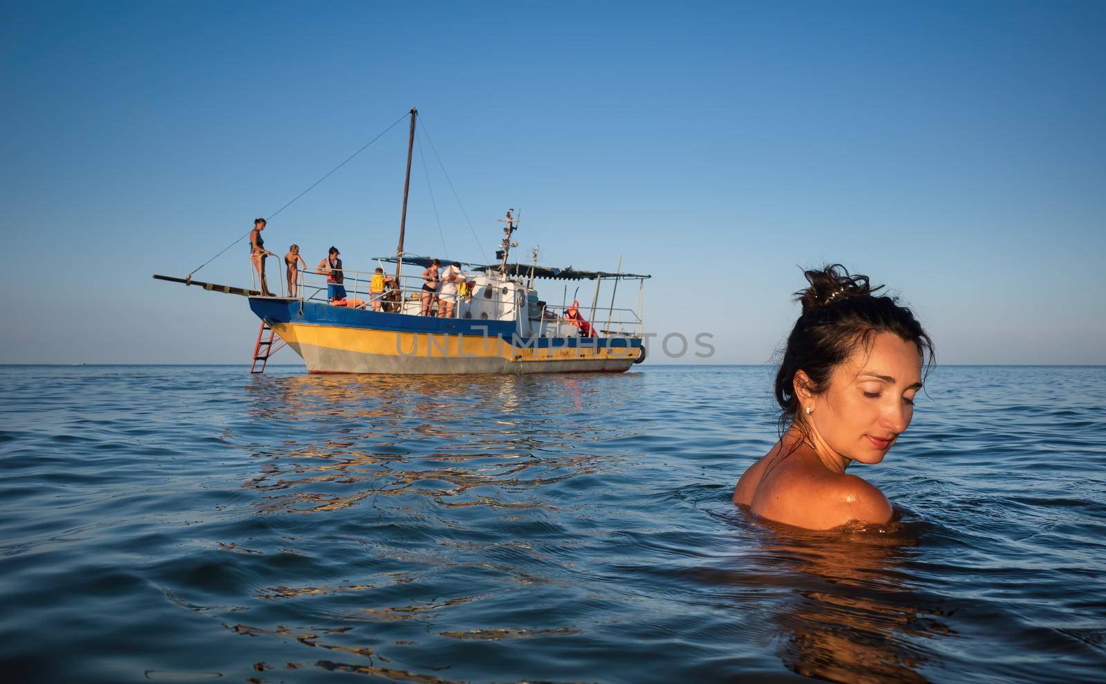 Relaxation and healthy lifestyle. Young beautiful and emotional woman swims in the sea on a sunny day. Boat in the background