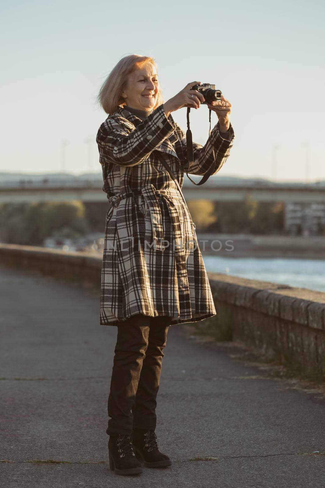 Senior woman enjoys photographing while standing by the river.