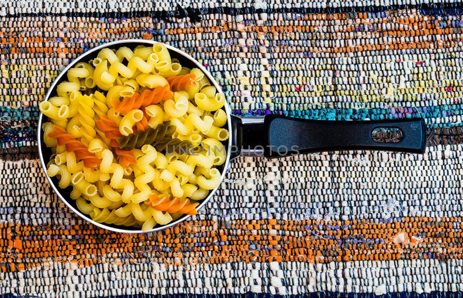 Small mini frying pan with tricolor raw fusilli pasta in a rustic composition.