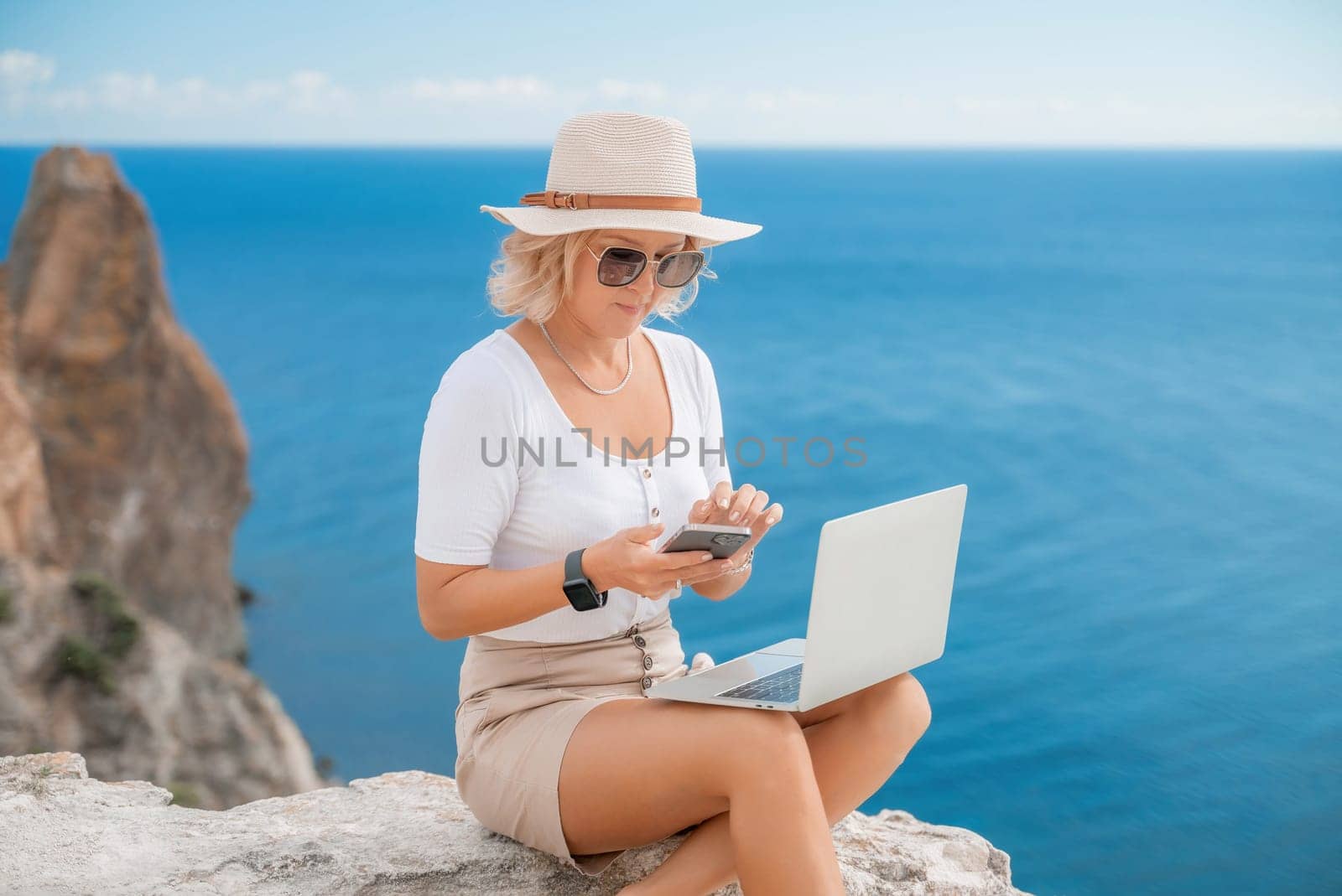 Freelance women sea working on the computer. Good looking middle aged woman typing on a laptop keyboard outdoors with a beautiful sea view. The concept of remote work. by Matiunina