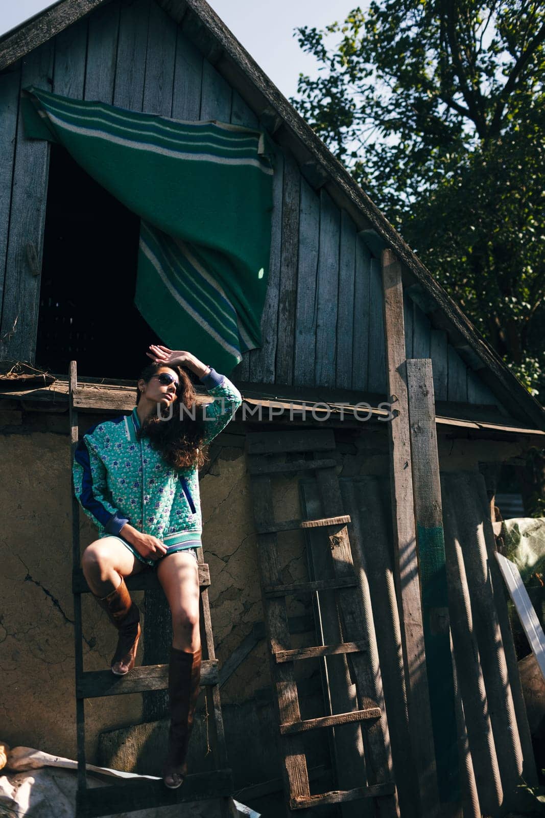 Conceived beautiful young woman on a wooden stepladder on the background of a old farm house. Women's housework concept