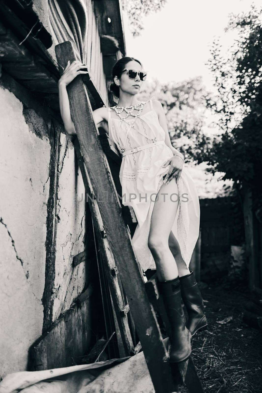 Tall gorgeous sexy brunette woman in white dress posing on wodden stepladder showing her perfect long legs and hip. Beauty of womans body and stylish look concept.