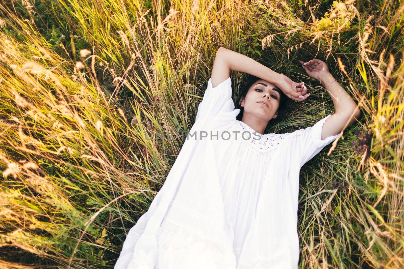 Conceived Beautiful young woman lying in the grass, wearing a white dress. Nature, summer holidays, vacation and people concept