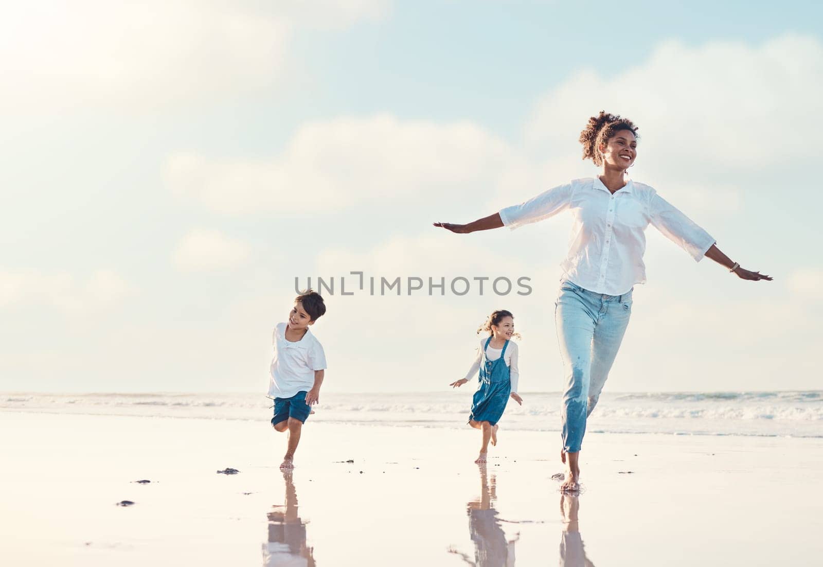 Mother, son and daughter on the beach to dance together while outdoor for travel or vacation in summer. Sunset, family or children and a woman having fun with her kids on the coast by the ocean.