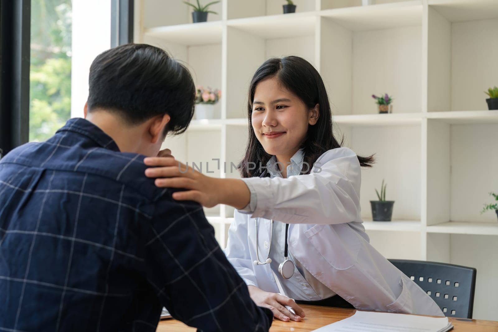 Asian female doctor giving hope and encourage to stressed man patient at hospital. Smiling doctor woman touching on patient shoulder to support take care and helping . Supported and Encouraged.