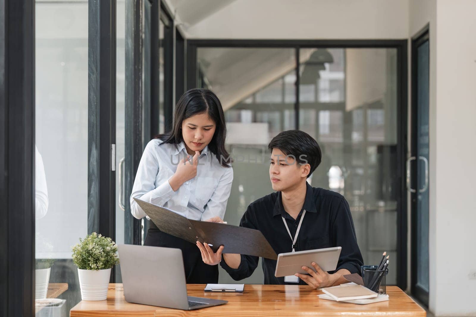 Two asian business worker looking at folder and discussing corporate strategy in teamwork, working on computer laptop in office at office.