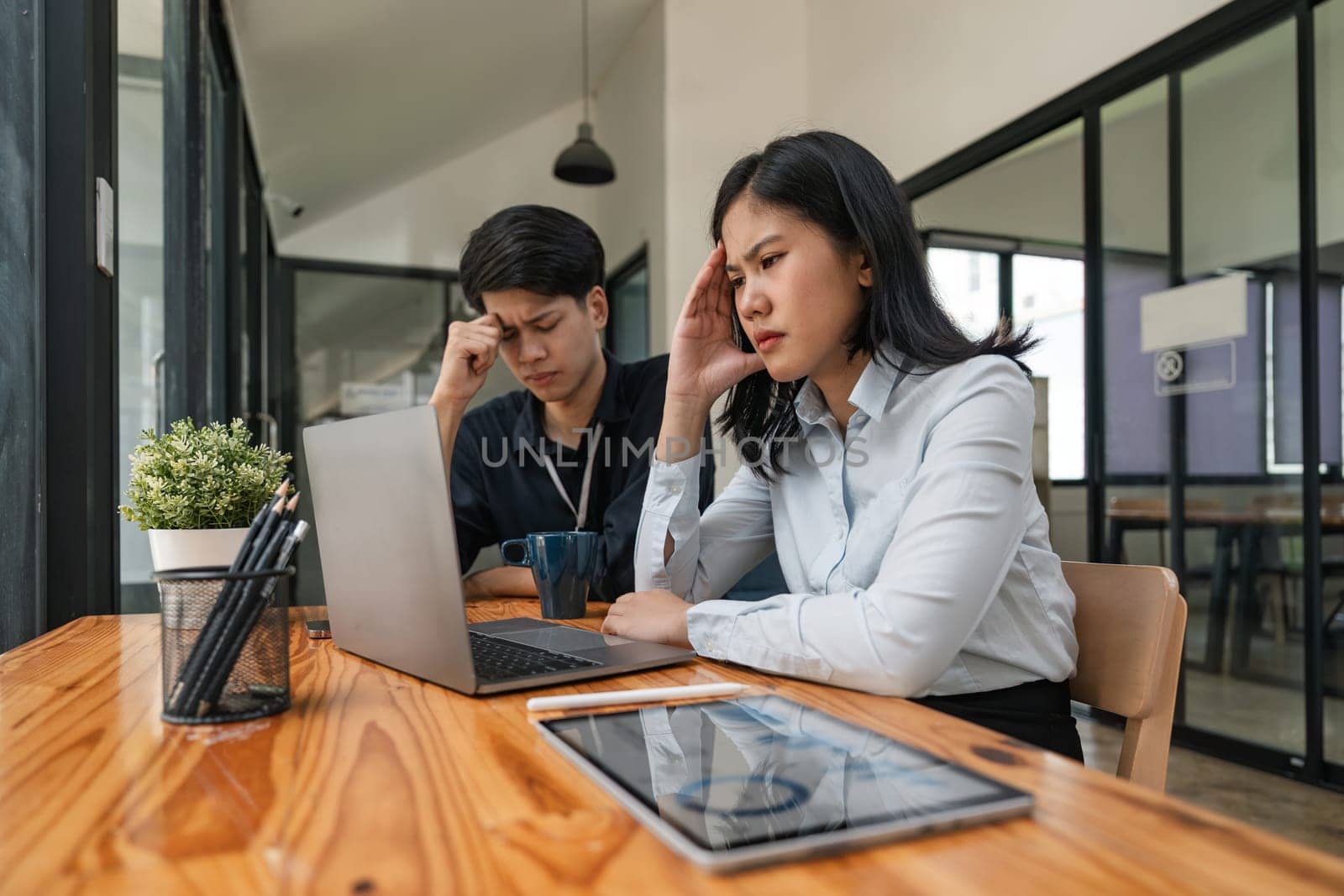 Two Asian business feeling migraine head strain. Overworked businesswoman financier while working on laptop and tablet at office.